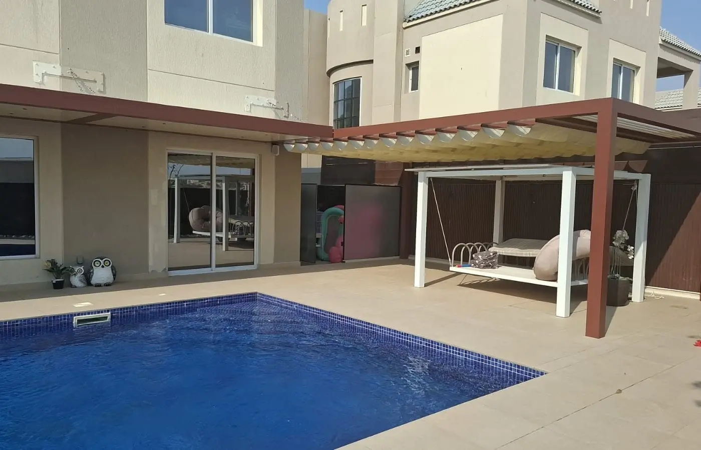Wall-mounted Nimbus pergola along a villa and Wave retractable shades over the garden beside the pool in Living Legends, Dubai