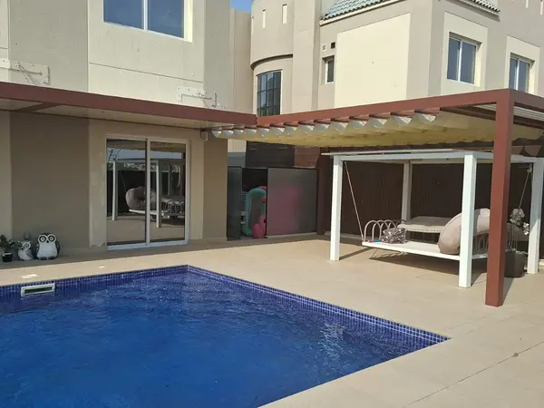 Wall-mounted Nimbus pergola along a villa and Wave retractable shades over the garden beside the pool in Living Legends, Dubai