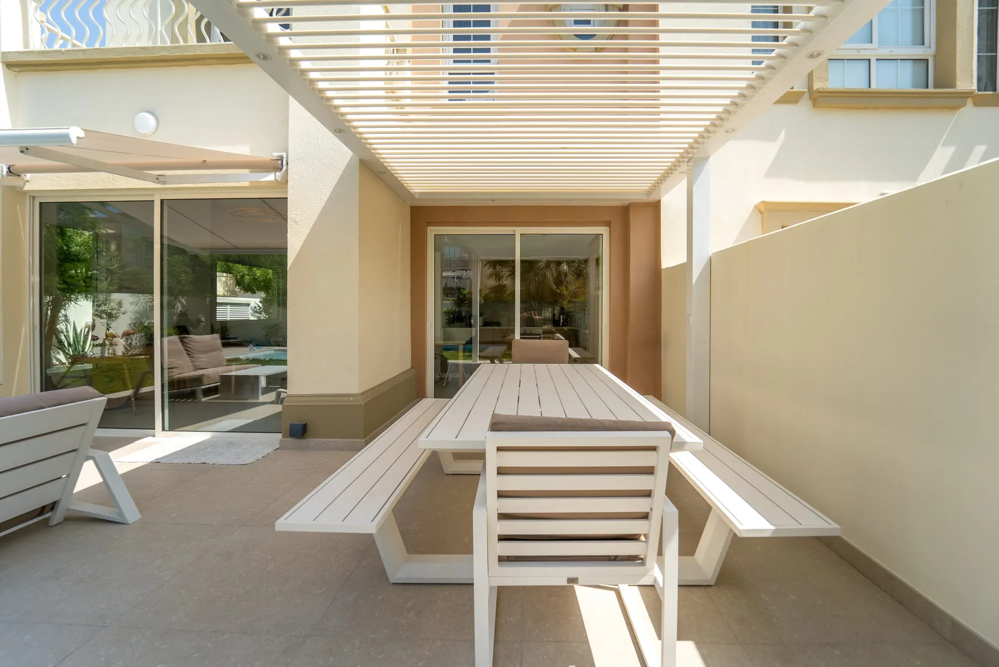 Outdoor dining table under the white fixed louvres of the Liwa pergola in The Springs